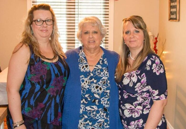 Three women wearing flower-patterned tops or dresses look into the camera.