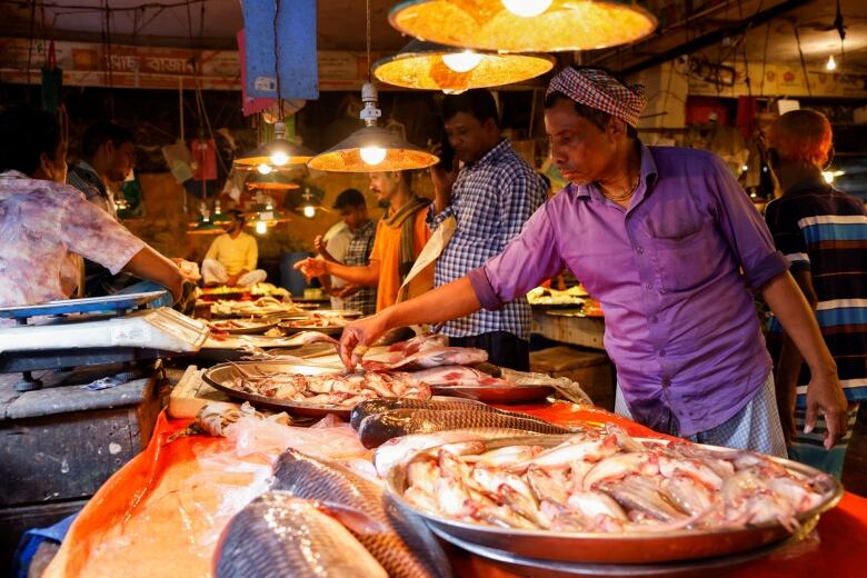 Sellers at a fish market with whole fish laid out in large round bowls