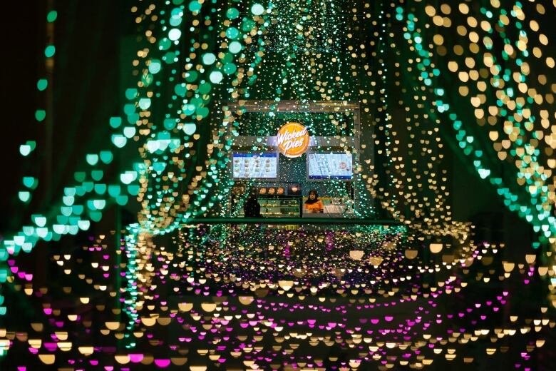 A shopkeeper at a stall is seen through strings of lights in green, yellow and purple colours ahead of Ramadan.