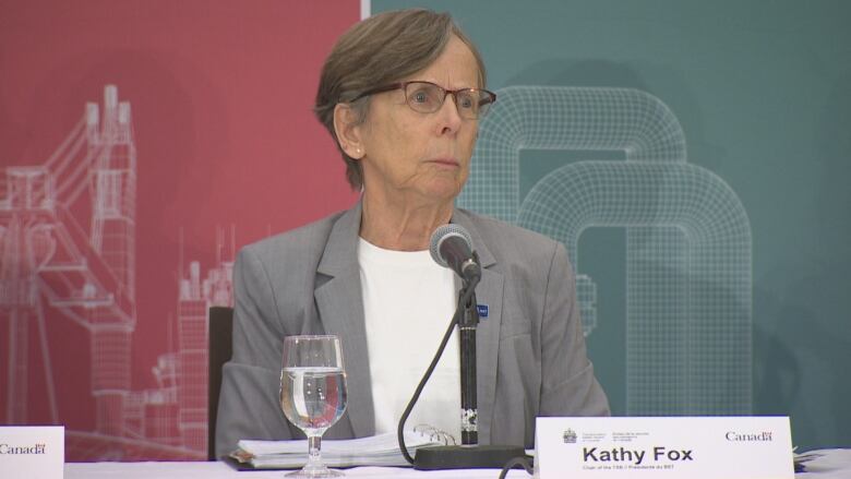 A woman in a grey blazer sits in front of a microphone.