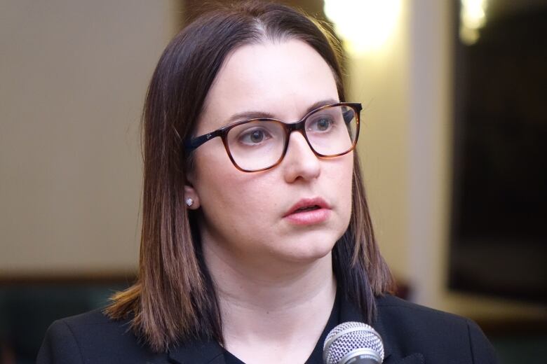 A a close-up of a person with long hair wearing glasses speaking into a microphone.