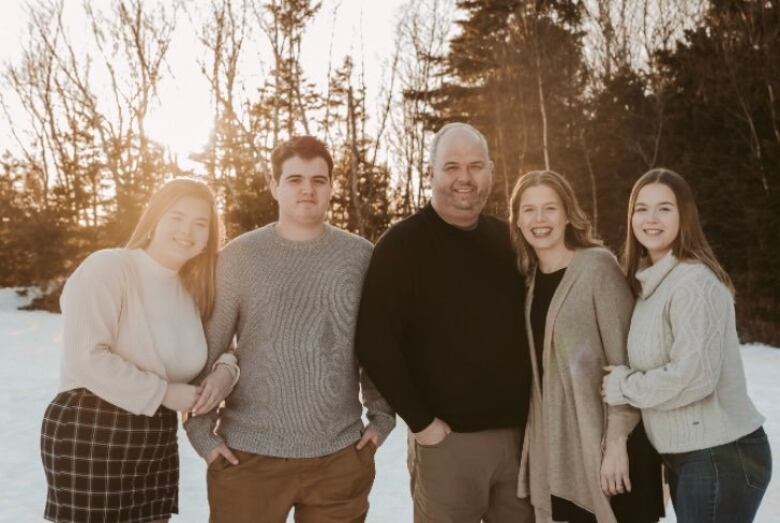 Two men and three women stand in front of a snowy field, with the sun shining behind them.