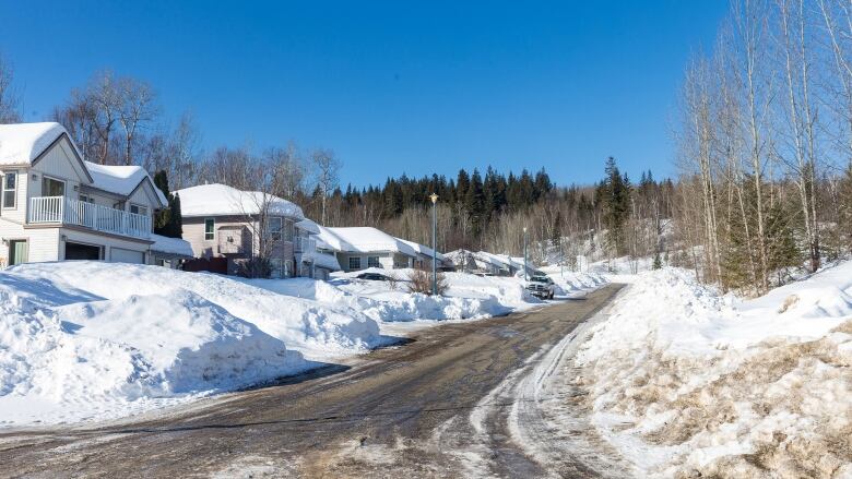 Snow-covered homes are seen on a rural street on a sunny day.