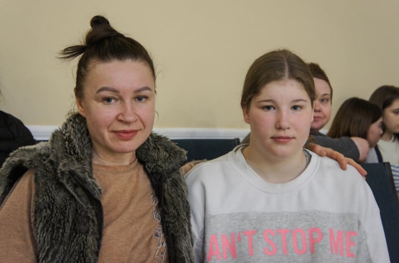 A mother wearing a fur vest with arm around her teenage daughter.