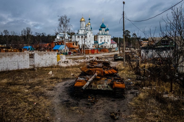 A tank parked in a a grassy area in front of white church buildings with gold and blue minarets on the top of the structures.