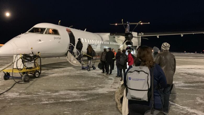 A line of people stand on a snowy runway leading to a Porter airplane with its stairs down