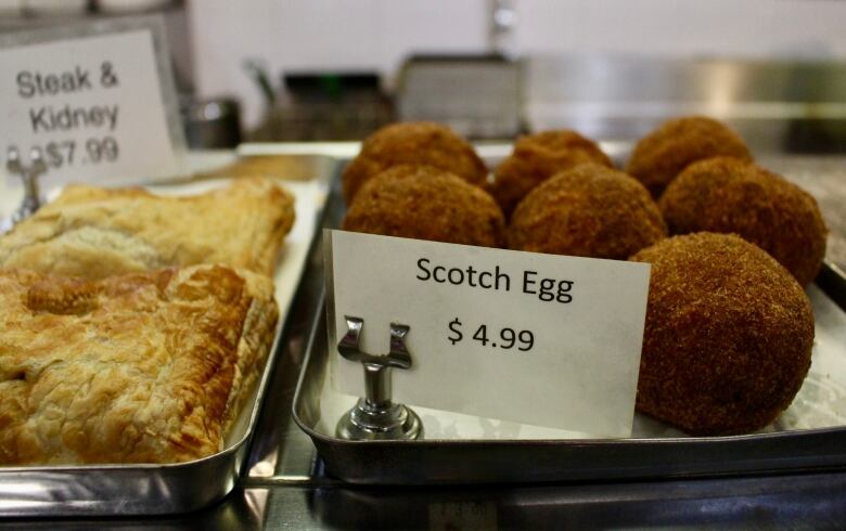 Round, deep-fried balls sit on a metal tray. A sign reads  