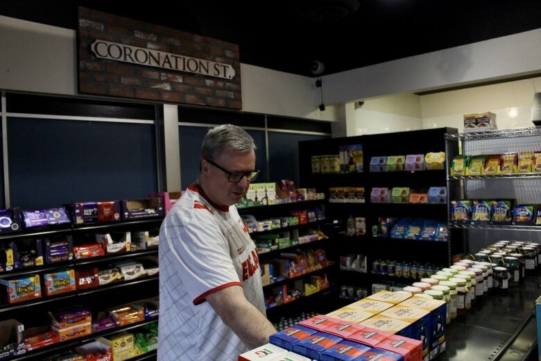 A man inspects grocery shelves stocked with colourful boxes, jars and other packages. A faux 