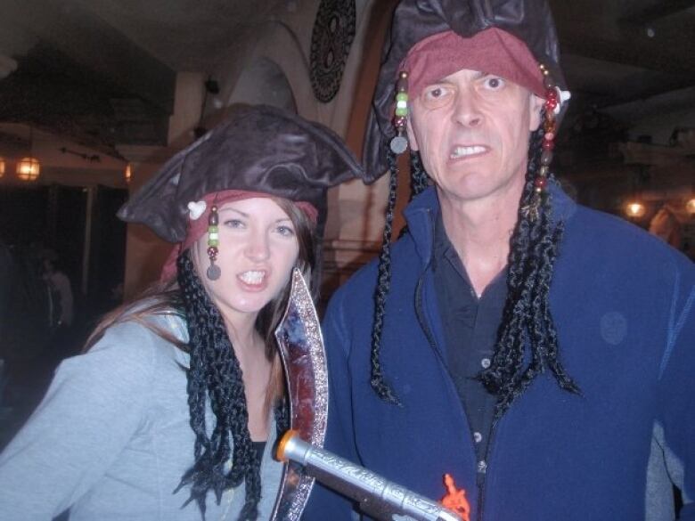 A young woman and man pose wearing pirate costume hats with beaded wigs and clenching their teeth. 