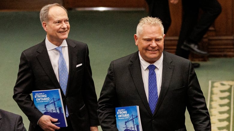 Two men hold budget books.