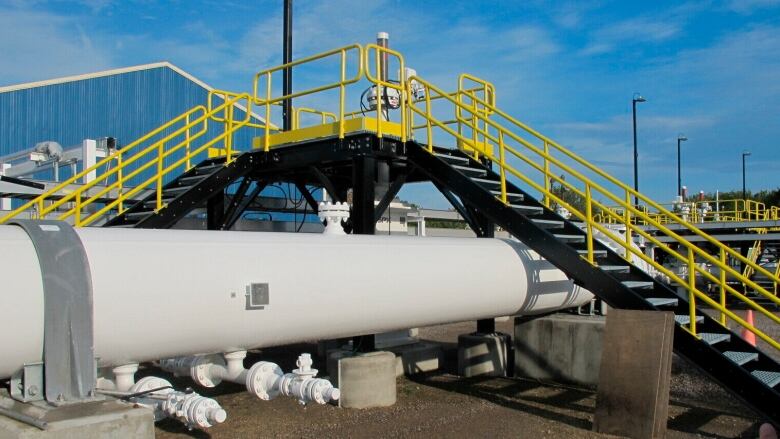 A set of stairs with yellow guard railings rises up and over a large grey pipeline.