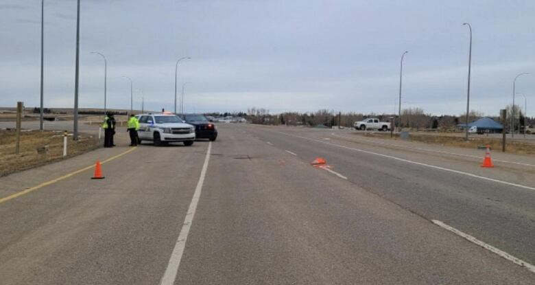 Police vehicles can be seen on the side of the highway along with several orange pylons, one of which, is squished, after it was driven over by a large truck.