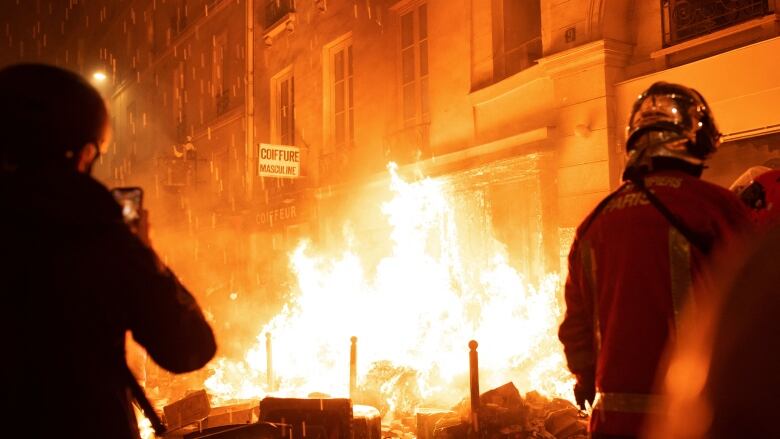 A large fire is shown in front of a building, with people in helmets in the foreground.