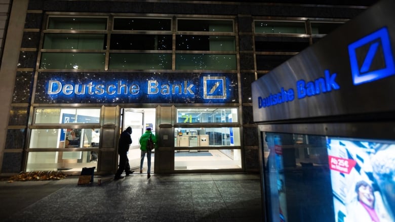 Silhouettes of shoppers are shown outside a Deutsche Bank branch in Berlin at night.