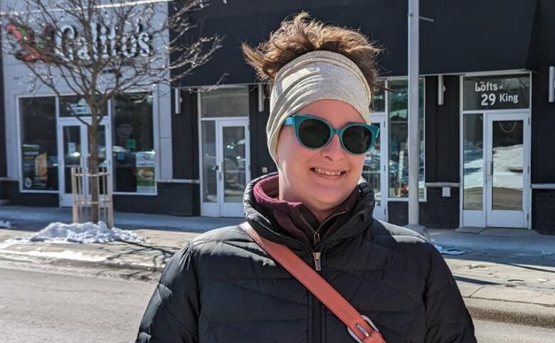 A woman stands at a bus stop with her hands in her pocket