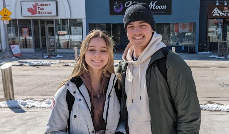 A teenage girl and boy stand smiling in front of store fronts on King St. in Kitchener.