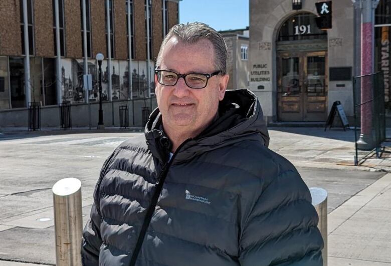 A man wearing glasses poses for a picture in front of Kitchener City Hall