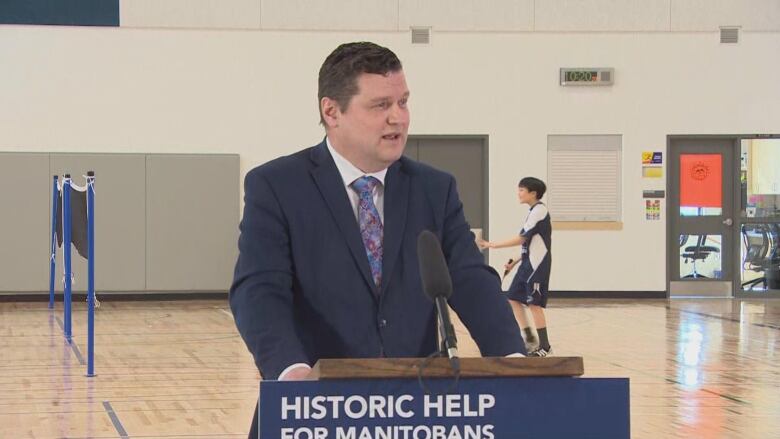 A man wearing a suit is speaking at a podium, with a sign that says 