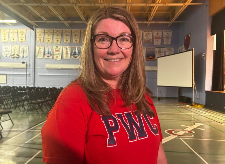 A woman wearing a red t shirt standing inside a high school gymnasium. 