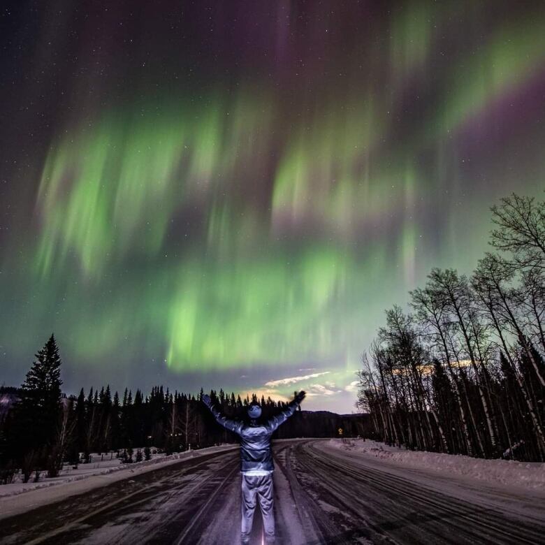 A man stands on the road with auroras overhead