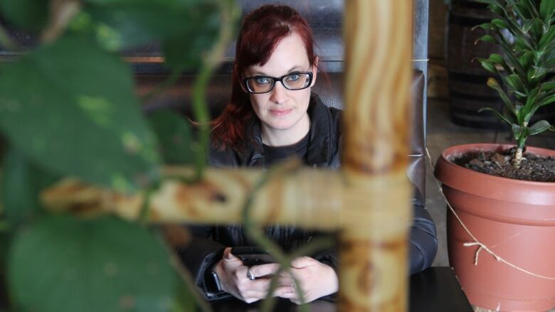 A woman sits at a booth, holding her phone. She is seen through the greenery decorations.