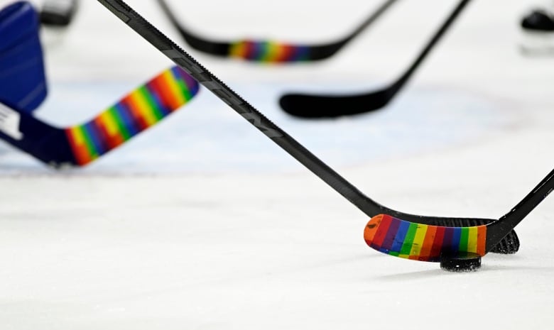 Hockey sticks wrapped in rainbow coloured-tape on the ice. 