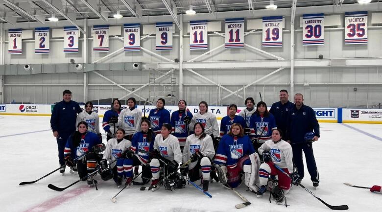 Hockey team poses on the rink with retired jerseys in the rafters