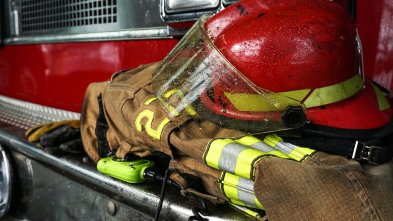 A brown firefighter's jacket and a red fire helmet sit on the bumper of a red fire truck.