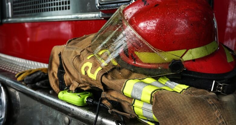 A brown firefighter's jacket and a red fire helmet sit on the bumper of a red fire truck.