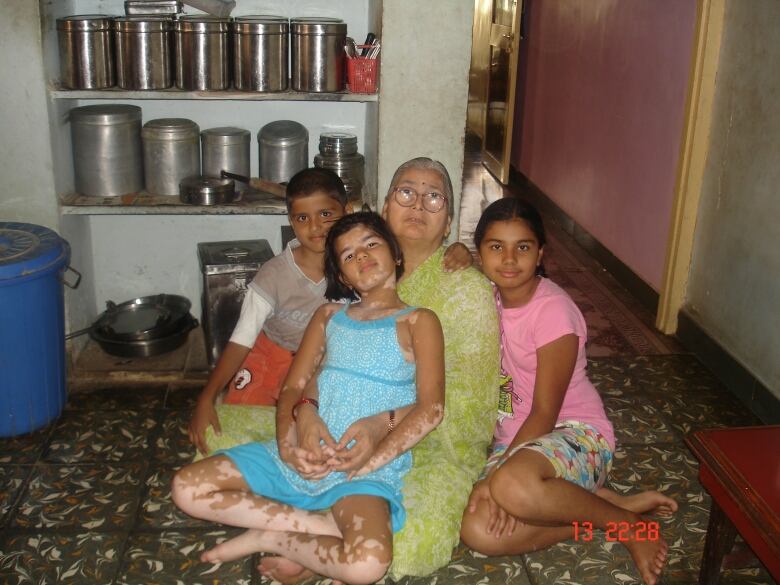 Three children sit on and beside a white-haired woman in a green sari.