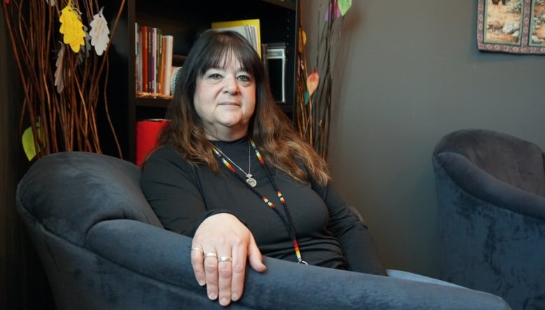 A woman with long brown hair sits in a blue-grey armchair.