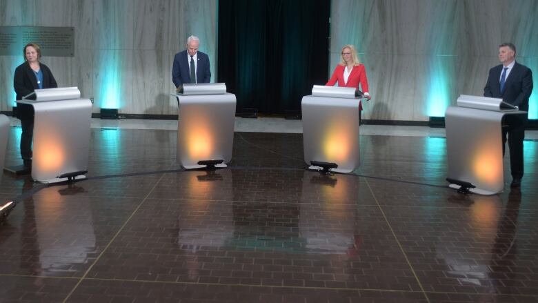 the four party leaders stand indoors at podiums