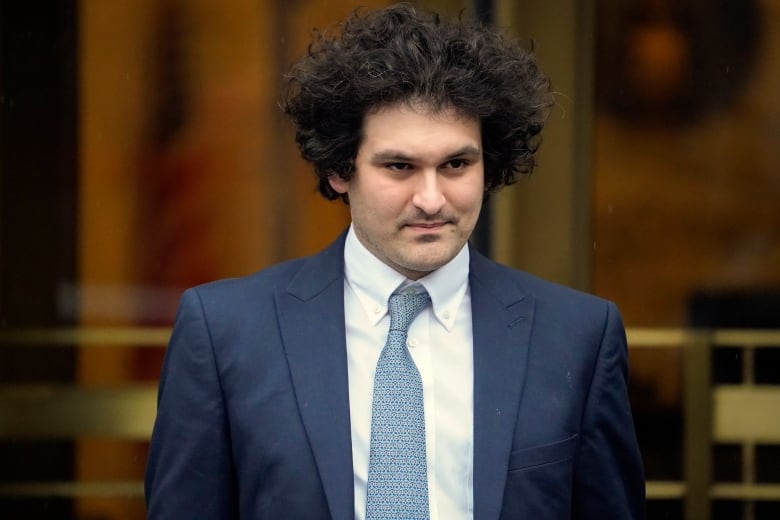 Sam Bankman-Fried, wearing a blue suit, white shirt and blue necktie, leaves a court in New York City.