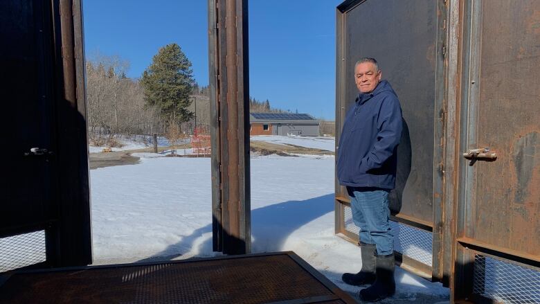 A man stands inside one of eight doors of a large metal firepit at kihcihkaw ask