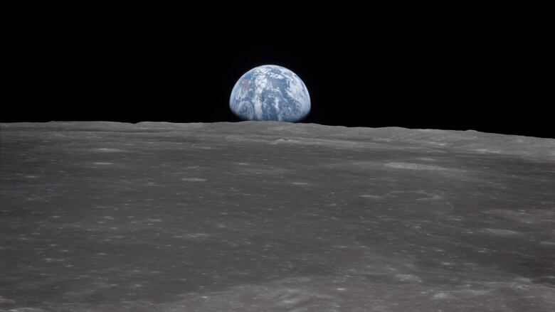 Earth is seen in the darkness of space, as seen from the horizon of the grey moon.