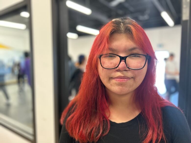 A teenage girl looks at the camera with black rim glasses and dyed red hair. 