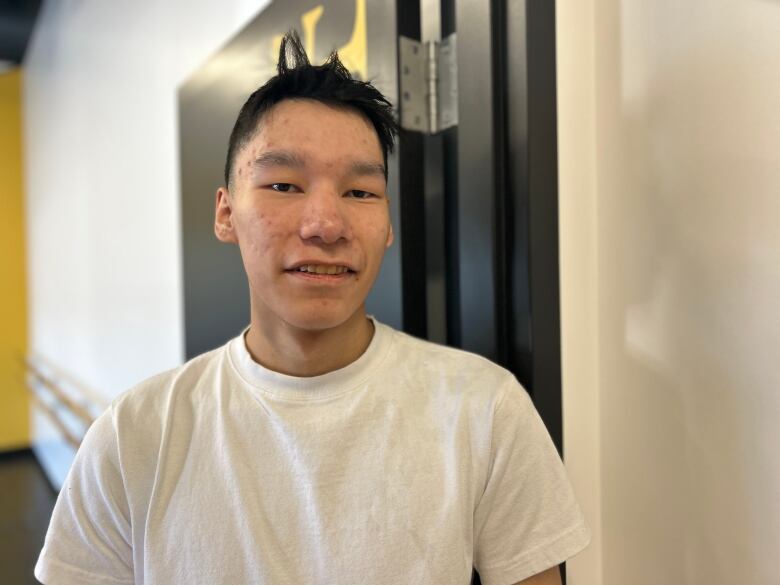 A teenage boy in a white t-shirt with black hair looks at the camera. 