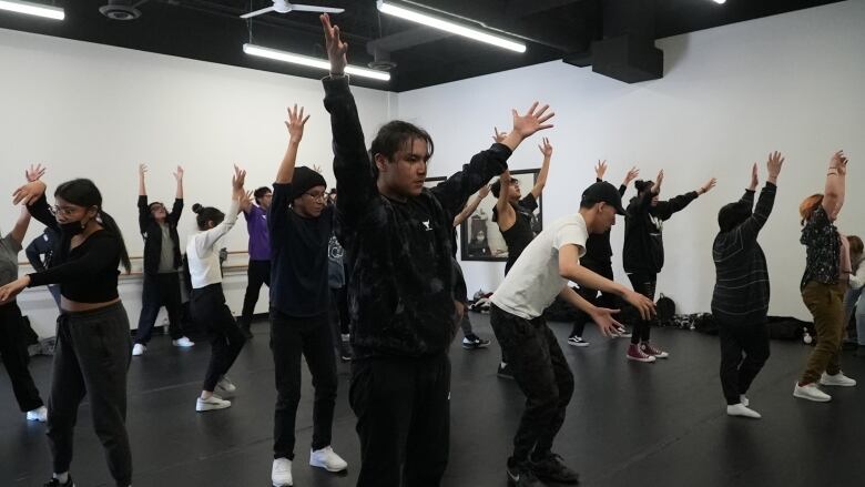 About a dozen students in the middle of a choreography lesson with their hands raised above their head. 