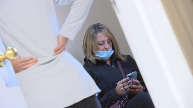 A woman holds a cell phone in her hands while sitting on a bench.