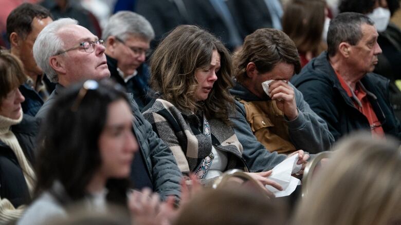 Several people are seen crying and wiping away tears while seated.