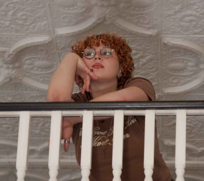 non-binary person with red curly hair stands in front of banister