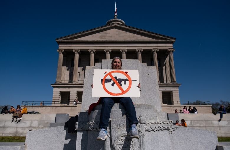 A protester in front of a government building holds a sign bearing the image of an assault rifle, crossed out.  