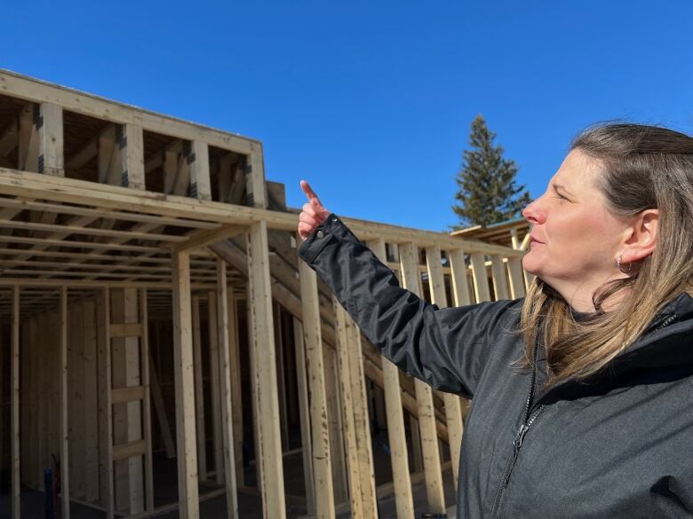 A woman in a jacket points at a new community hall being constructed.