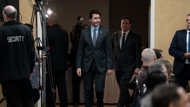 Two men in suits walk next to a man in a police jacket.