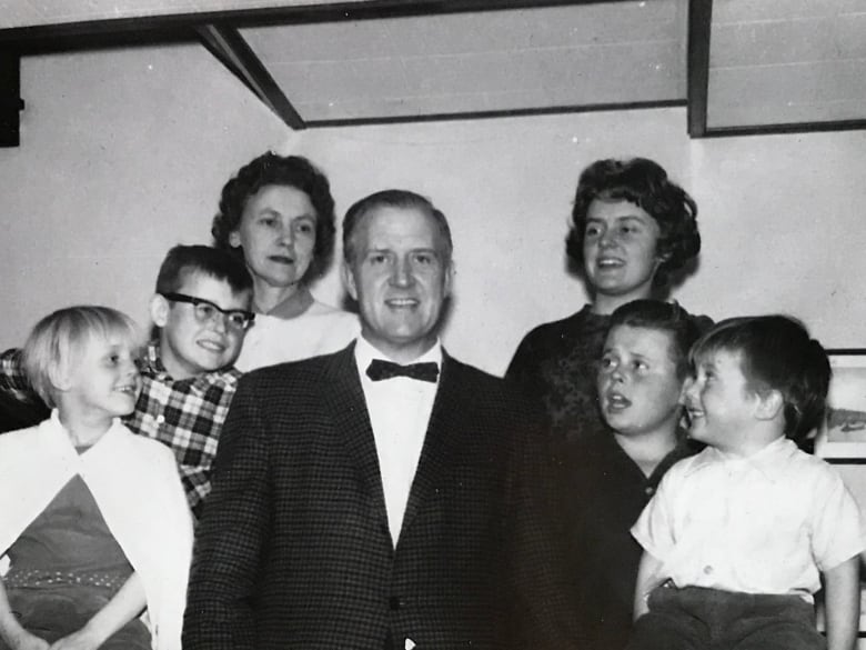 A man stands with a two women and four children around him in a black-and-white photo. 