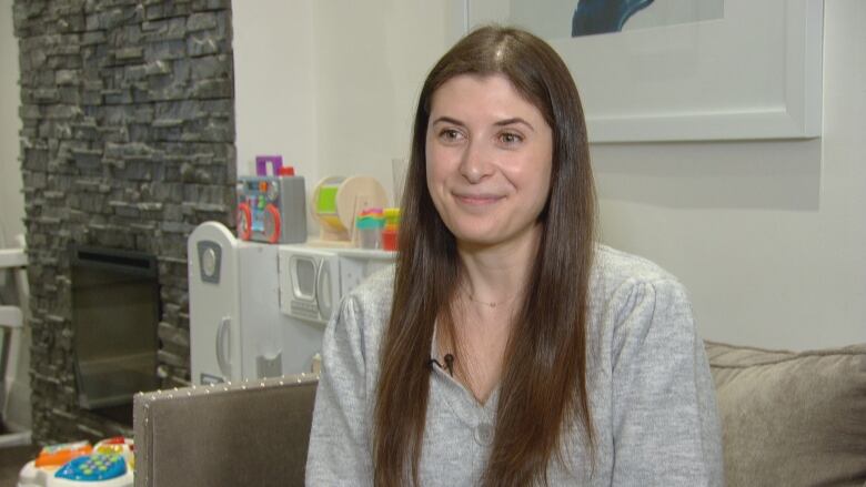 Alanna Handelman sitting on a couch with a slight smile. Children's toys are visible in the background. 