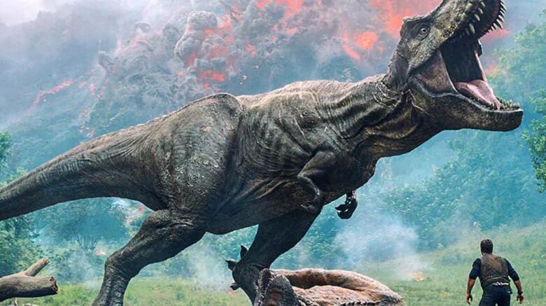 An aggressive T. rex shows all its teeth while a man cowers in fear in the movie Jurassic Park: Fallen Kingdom.