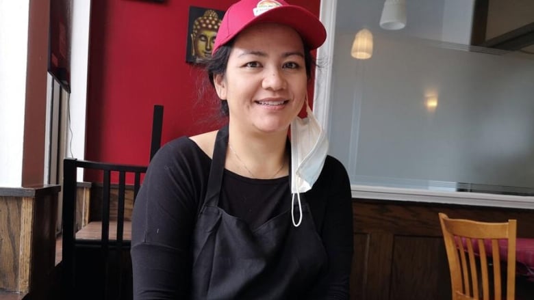 A young woman wearing a baseball cap sits in front of a table with three plates of food.