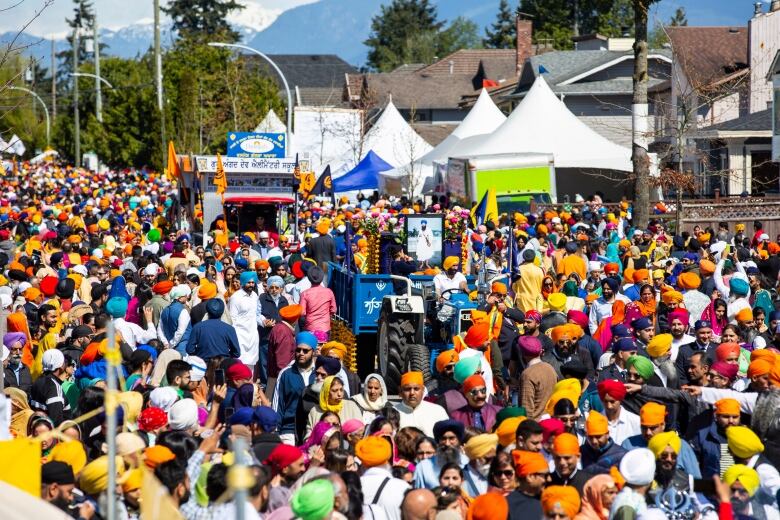 A gathering of people along a street in Surrey, B.C. during Vaisakhi wearing orange, blue and white.