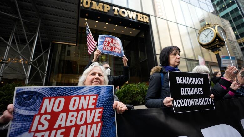 Several people with signs are shown gathering in front of an office tower.